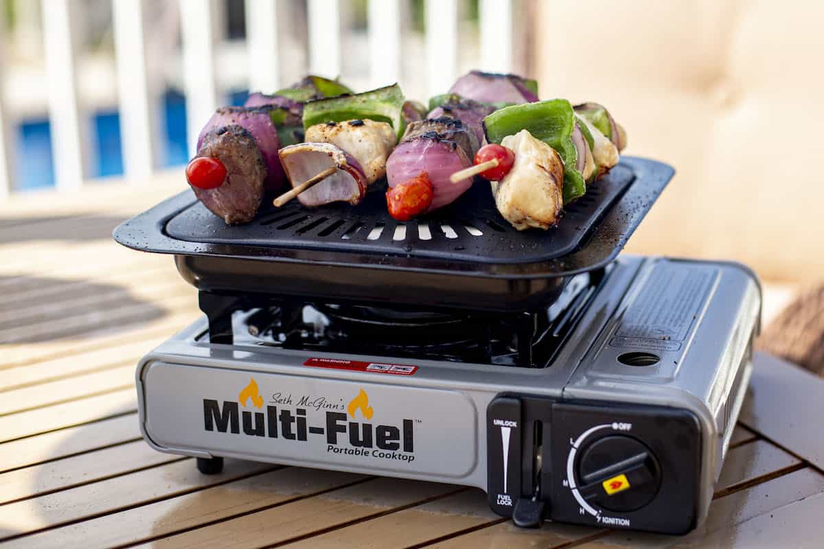 Multi-Fuel Portable Cooktop grilling skewers with vegetables and meat, showcasing The Tailgate Kit's outdoor cooking capabilities.